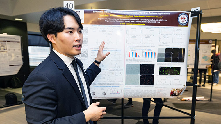 Missouri State student standing in front of their poster presentation explaining their research. 